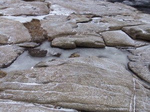 Pools of sea spray are frozen tight in the crevices of boulders overlooking the water.