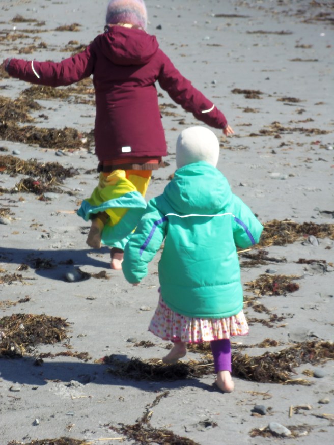 Bundled up and barefoot, two girls sprint along the ocean.
